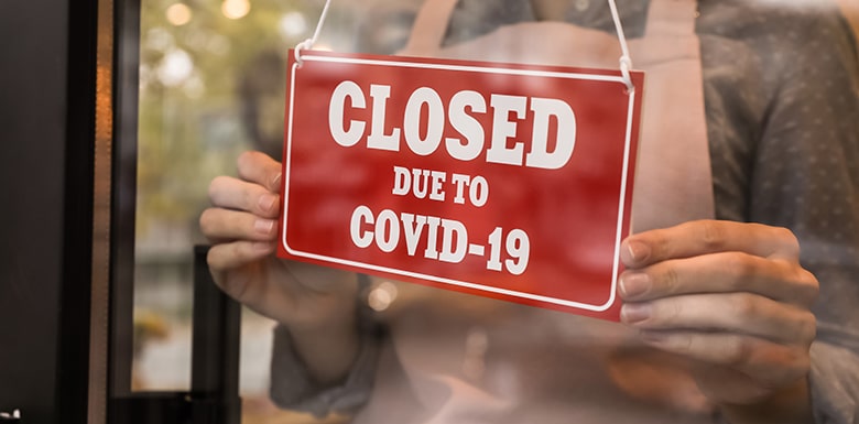 Small business putting up sign in door that reads CLOSED due to Covid-19