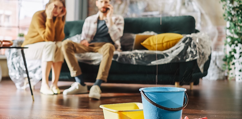 Couple sitting on a couch in their apartment with buckets on the floor catching dripping water