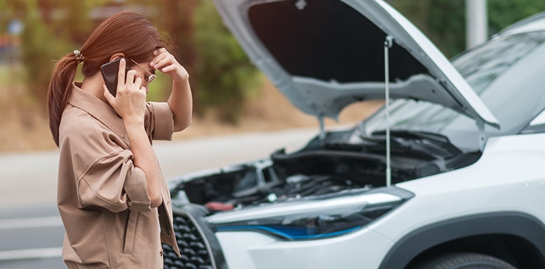 Frustrated woman talking on the phone while standing next to new car with hood popped open